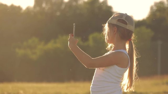 Cute girl teenager taking pictures of herself. Young beautiful girl doing selfie on mobile phone at sunset. Young girl doing selfie on sunset background.