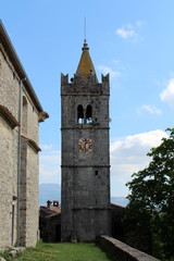 Fototapeta na wymiar Large stone bell tower with yellow top and rusted old metal clock in the middle