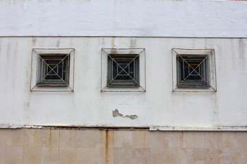 Fototapeta premium Three wooden frame rectangle glass windows with partially rusted metal bars mounted on dilapidated wall outside