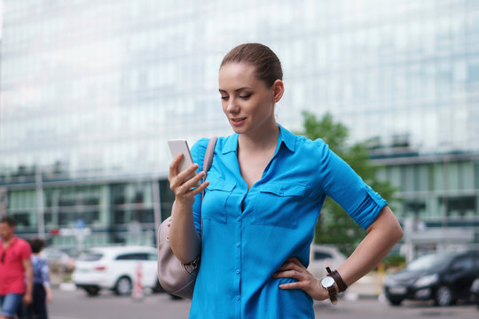 Young attractive girl is holding a cell phone. She looks at the smartphone screen and smiles. Good news