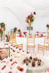Beautiful banquet hall under a tent for a wedding reception. Interior of a wedding tent decoration ready for guests. Decor flowers. Red theme