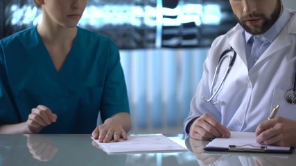 Female intern giving bribe to chief medical officer filling medical report