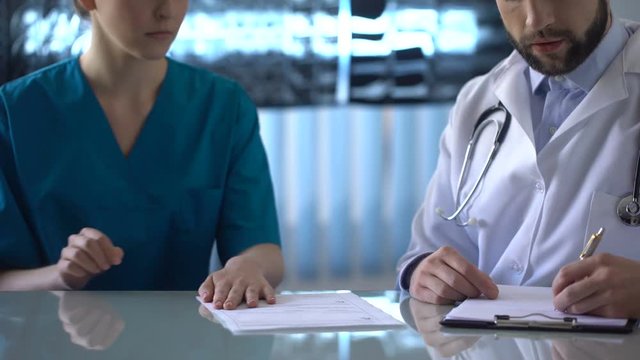 Female intern giving bribe to chief medical officer filling medical report