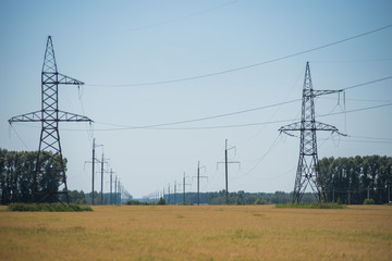 high voltage electrical power line in the field. High voltage lines and power pylons in a yellow rice field agricultural landscape on a sunny day with the blue sky
