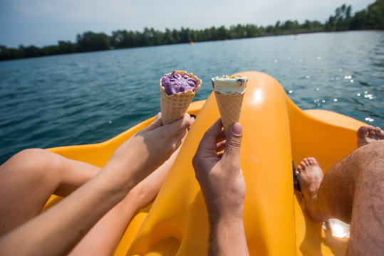 A couple of resting on a pedal boat on the lake. legs of men and women standing on the pedals of the boat. a couple have ice cream on a catamaran