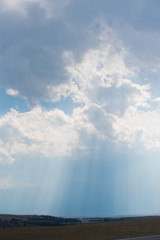 Naklejka na ściany i meble Clouds and a blue sky with a sunbeam shining through. Sun rays bursting through the clouds.