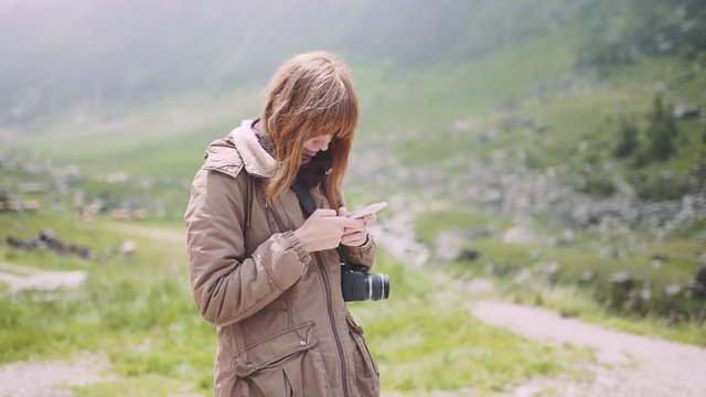 A young woman hiker climbs mountains with camera and use smartphone. Transfagarasan, Carpathian mountains in Romania