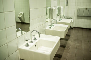 Male public toilet with white stylish sinks and urinal reflecting in mirror