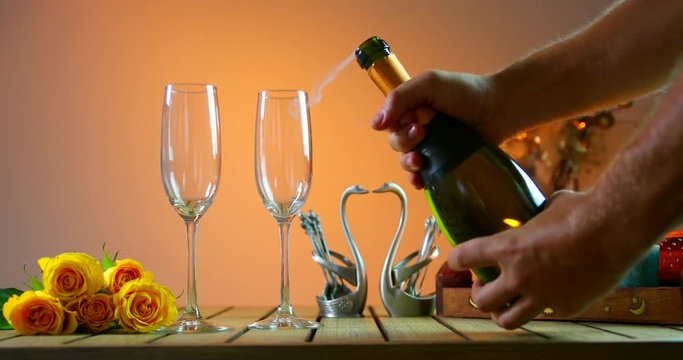 Bottle of champagne opening.С ork flies out. Two glasses. Man pours champagne into glasses. Romantic evening.