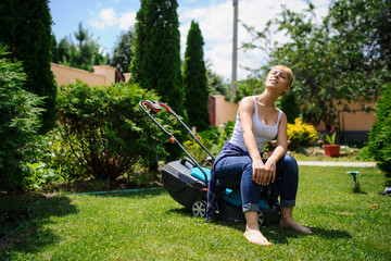 Gardener girl is cutting the grass with the mower - obrazy, fototapety, plakaty