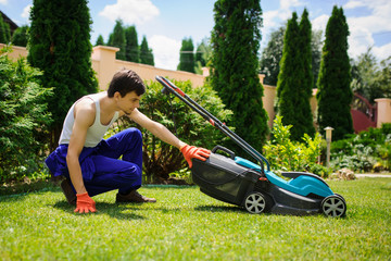 Fototapeta na wymiar Gardener man is cutting the grass with the mower