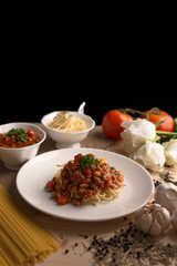 Delicious spaghetti with various spices, garlic, pepper, oregano, parsley and white roses on isolated black background.