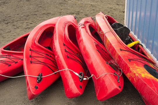 Empty red plastic recreational kayaks for rent or hire, stored on sandy beach after hours on a rainy day. Crescent Beach, Surrey, British Columbia, Canada.