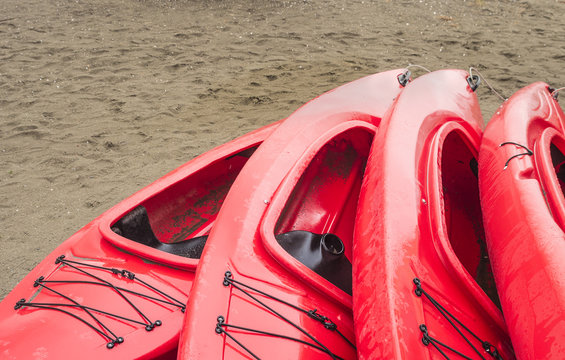 Empty red plastic recreational kayaks for rent or hire, stored on sandy beach after hours on a rainy day. Crescent Beach, Surrey, British Columbia, Canada.