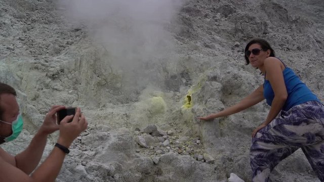 A man is taking pictures of a woman next to a fumarole on a smartphone