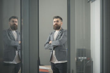 Confidence and success concept. Bearded man look out room door. Businessman in modern office with glass walls. Confident man in casual suit at working place. Business and office lifestyle