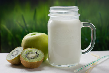 Smoothies in a glass jar, sliced kiwi on a green background