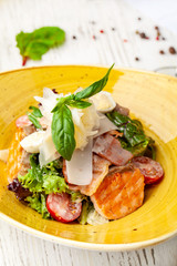 Caesar salad with salmon. mix of salads, cherry tomatoes, parmesan cheese, basil. A dish in a ceramic plate is on a wooden table in a restaurant. A glass of white wine is on the table. selective focus