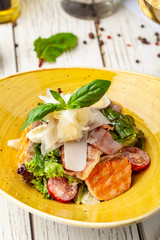 Caesar salad with salmon. mix of salads, cherry tomatoes, parmesan cheese, basil. A dish in a ceramic plate is on a wooden table in a restaurant. A glass of white wine is on the table. selective focus