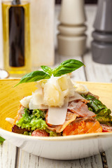 Caesar salad with salmon. mix of salads, cherry tomatoes, parmesan cheese, basil. A dish in a ceramic plate is on a wooden table in a restaurant. A glass of white wine is on the table. selective focus