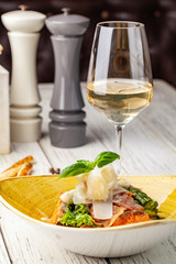 Caesar salad with salmon. mix of salads, cherry tomatoes, parmesan cheese, basil. A dish in a ceramic plate is on a wooden table in a restaurant. A glass of white wine is on the table. selective focus