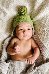 A newborn baby in a hat lies in a crib.