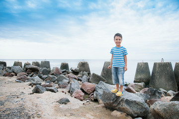 Boy in a striped T-shirt at the seaside breakwater block. boy standing on the beach. kid stands on...