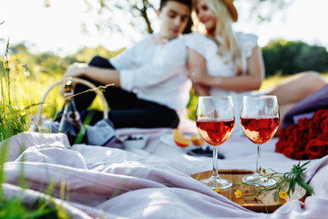 love, dating, people and holidays concept - happy couple on picnic over sunset background. Two glass of champain