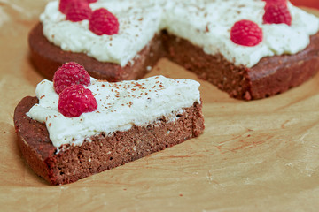 Piece of gluten free flour-less chocolate dates cake with whipped cream and raspberry topping.