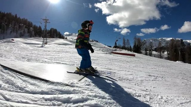 Freestyle skiing. Little boy jumping in a snowpark. A 5 year old child enjoys a winter holiday in the Alpine resort. Stabilized shot. Slow motion.