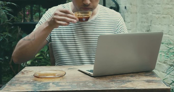 Young man drinking coffee and working on laptop outdoors