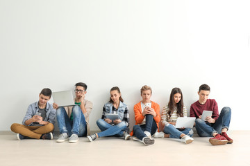 Group of teenagers with modern devices sitting on floor near wall