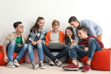Group of teenagers with modern devices sitting near white wall
