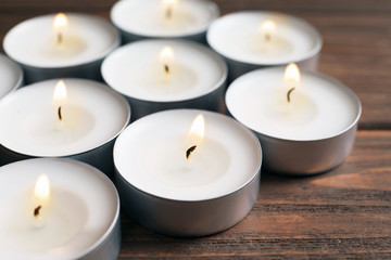 Small wax candles burning on wooden table, closeup