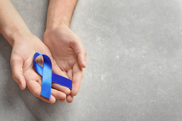 Man holding blue ribbon on grey background. Cancer awareness