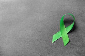 Green ribbon on grey background. Cancer awareness