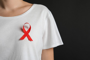 Woman with red ribbon on t-shirt against black background. Cancer awareness