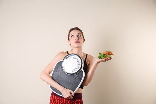 Young beautiful woman with scales and sandwich on light background. Weight loss motivation