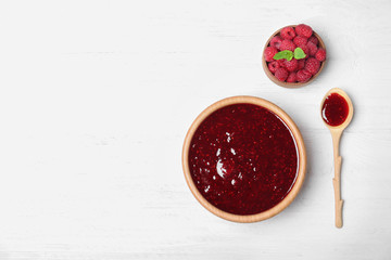 Bowl and spoon with delicious raspberry jam on wooden table, top view