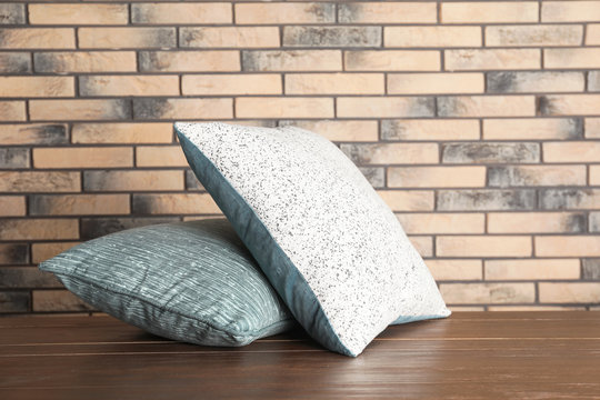 Soft decorative pillows on table against brick wall background