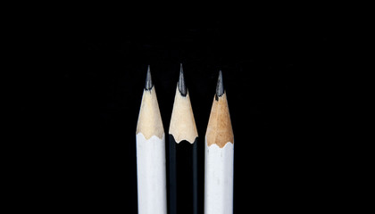 Three sharpened black and white pencils on black background.