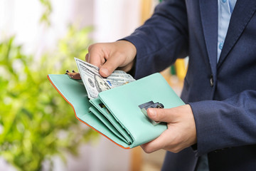 Woman taking out cash from stylish wallet on blurred background, closeup