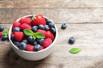 Bowl with raspberries, strawberries and blueberries on wooden table