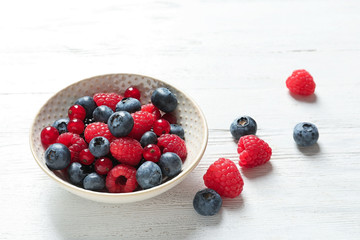 Bowl with raspberries, red currant and blueberries on wooden table
