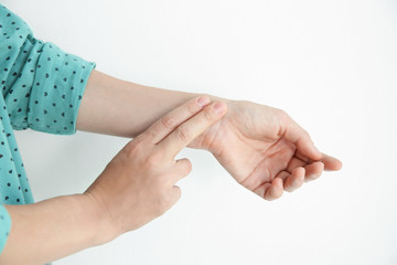 Young woman checking pulse on light background