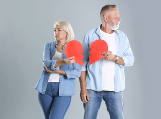 Mature couple with torn paper heart on grey background. Relationship problems