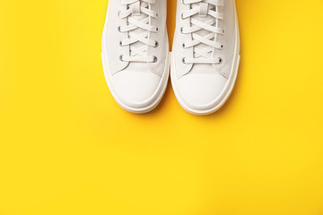 Pair of white sneakers on color background, top view