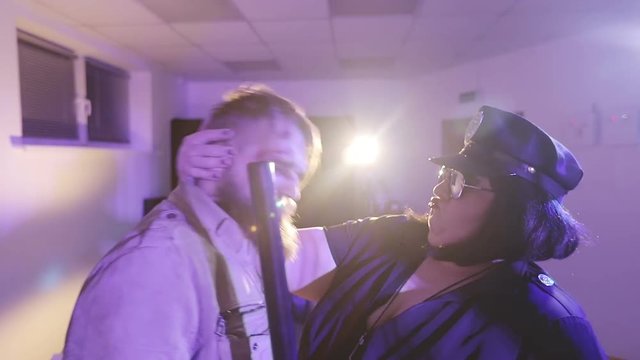 A wounded man with a beard and a fat police woman are having fun in the prison cell