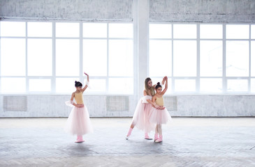 Naklejka premium Teacher trains ballet moves with little girls in pink clothes in the room