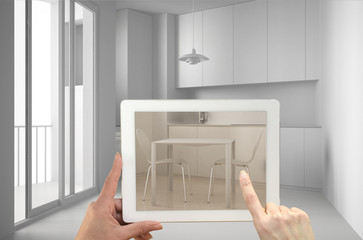 Augmented reality concept. Hand holding tablet with AR application used to simulate furniture and interior design products in real home, minimalist kitchen with dining table